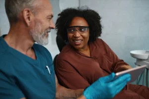 A imagem mostra um dentista de meia-idade atendendo uma paciente.
