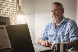 A imagem mostra um homem de meia-idade, utilizando o laptop, enquanto está sentado. Ilustra o texto sobre Como comprovar vínculo empregatício que não consta no INSS.