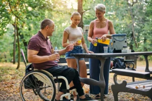 A imagem mostra um homem de meia idade, cadeirante, aproveitando um picnic ao ar livre, com sua filha e mulher. Os três sorriem. Ilustra o texto sobre aposentadoria para PCD.