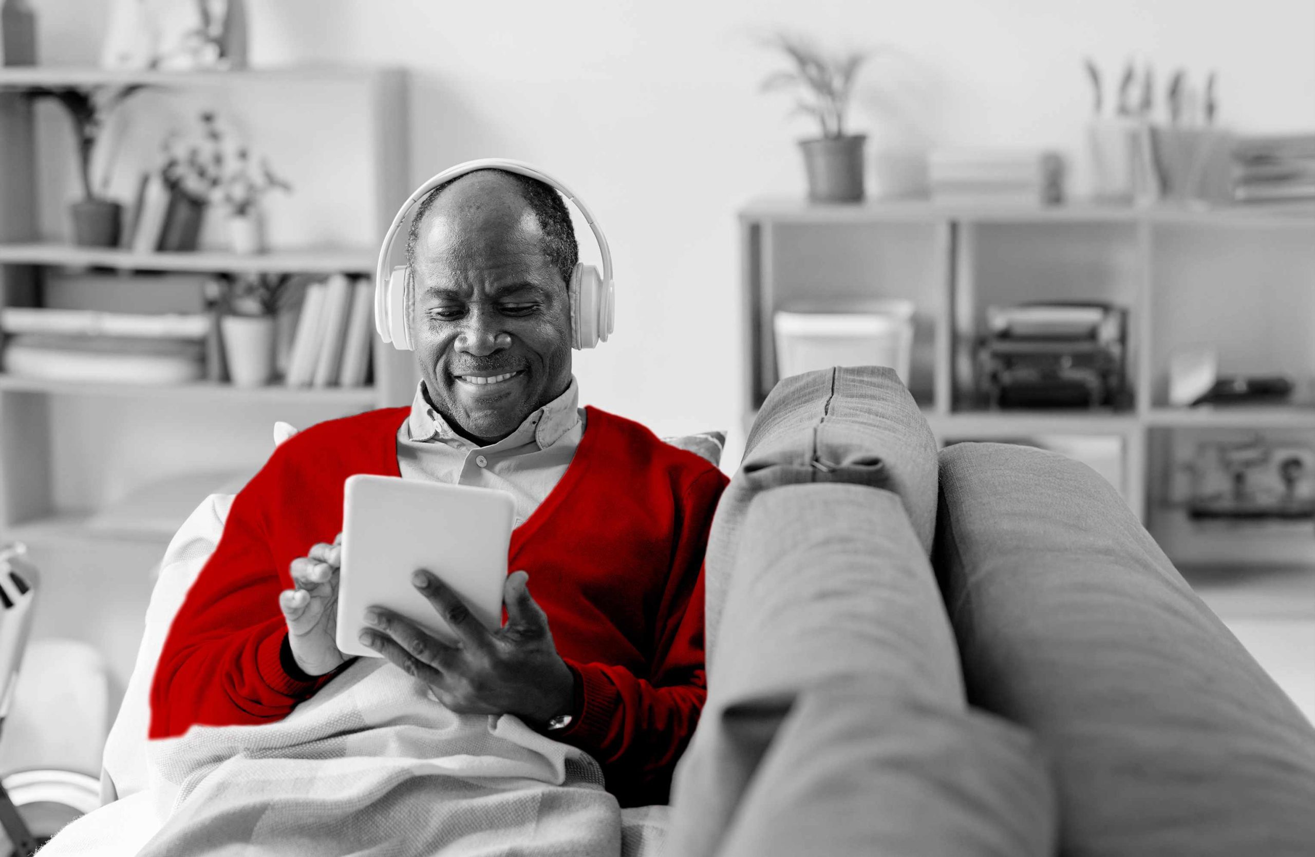 A imagem mostra um homem sorrindo, sentado no sofá com um tablet