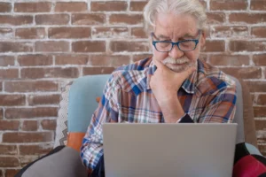 A imagem mostra um homem sênior, de cabelos brancos, concentrado, enquanto utiliza o laptop. Ilustra o texto sobre revisão no INSS.