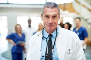 A imagem mostra um médico de meia idade, em ambiente hospitalar, sorrindo para a câmera. Ilustra o texto sobre modelo de PPP.