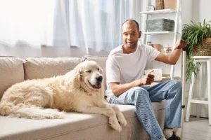 A imagem mostra um homem de meia idade, com visão monocular, sentando em seu sofá, ao lado de seu cachorro. Ilustra o texto sobre visão monocular na aposentadoria.