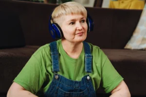 A imagem mostra uma mulher de meia idade, com cabelos curtos loiros, com fones de ouvido. Ilustra o texto sobre autismo pcd.