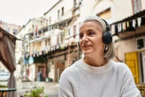A imagem mostra uma mulher sênior, ao ar livre, com fones de ouvido (abafadores). Ilustra o texto sobre autista aposenta.