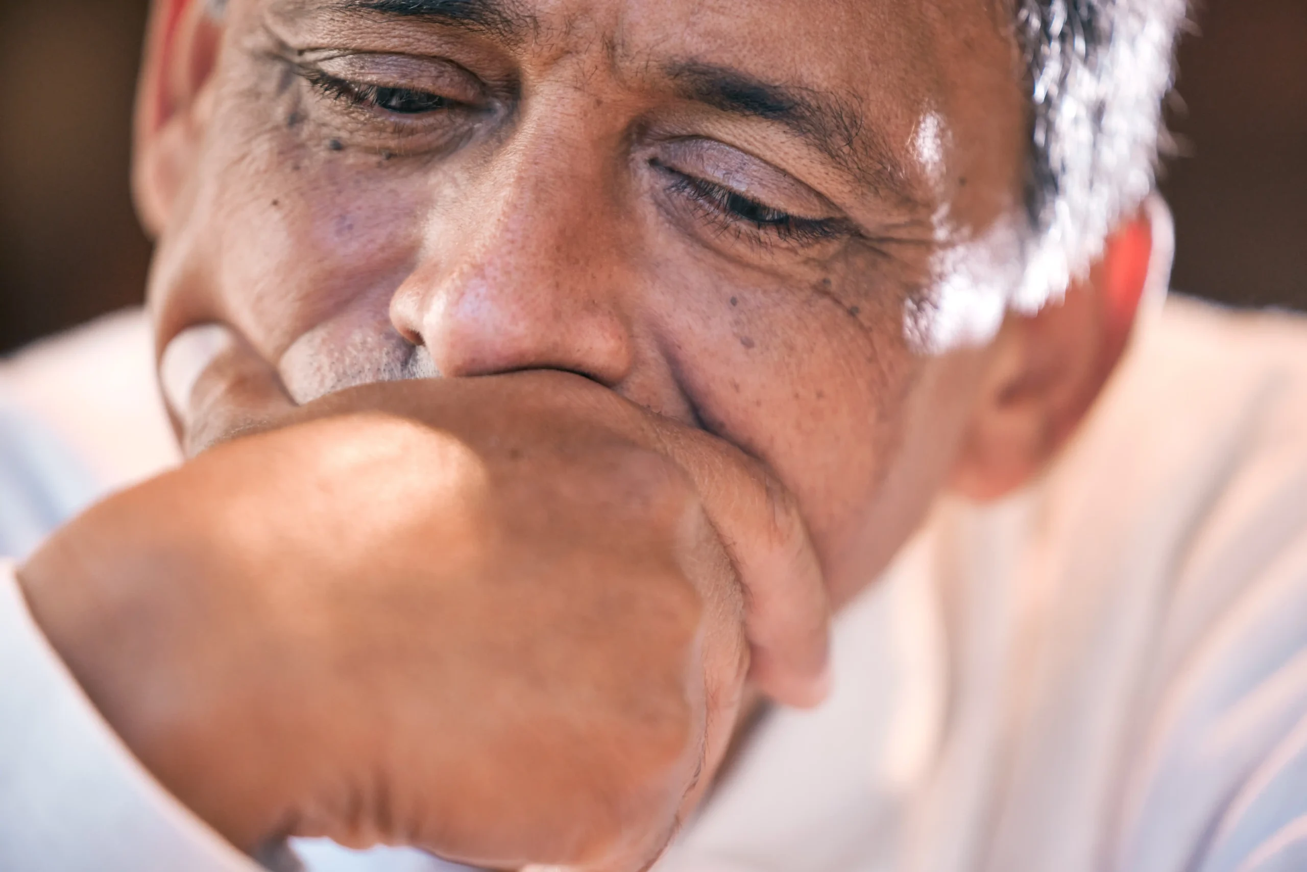 A imagem mostra em destaque, o rosto de um homem de meia-idade, reflexivo, com uma das mãos na boca.