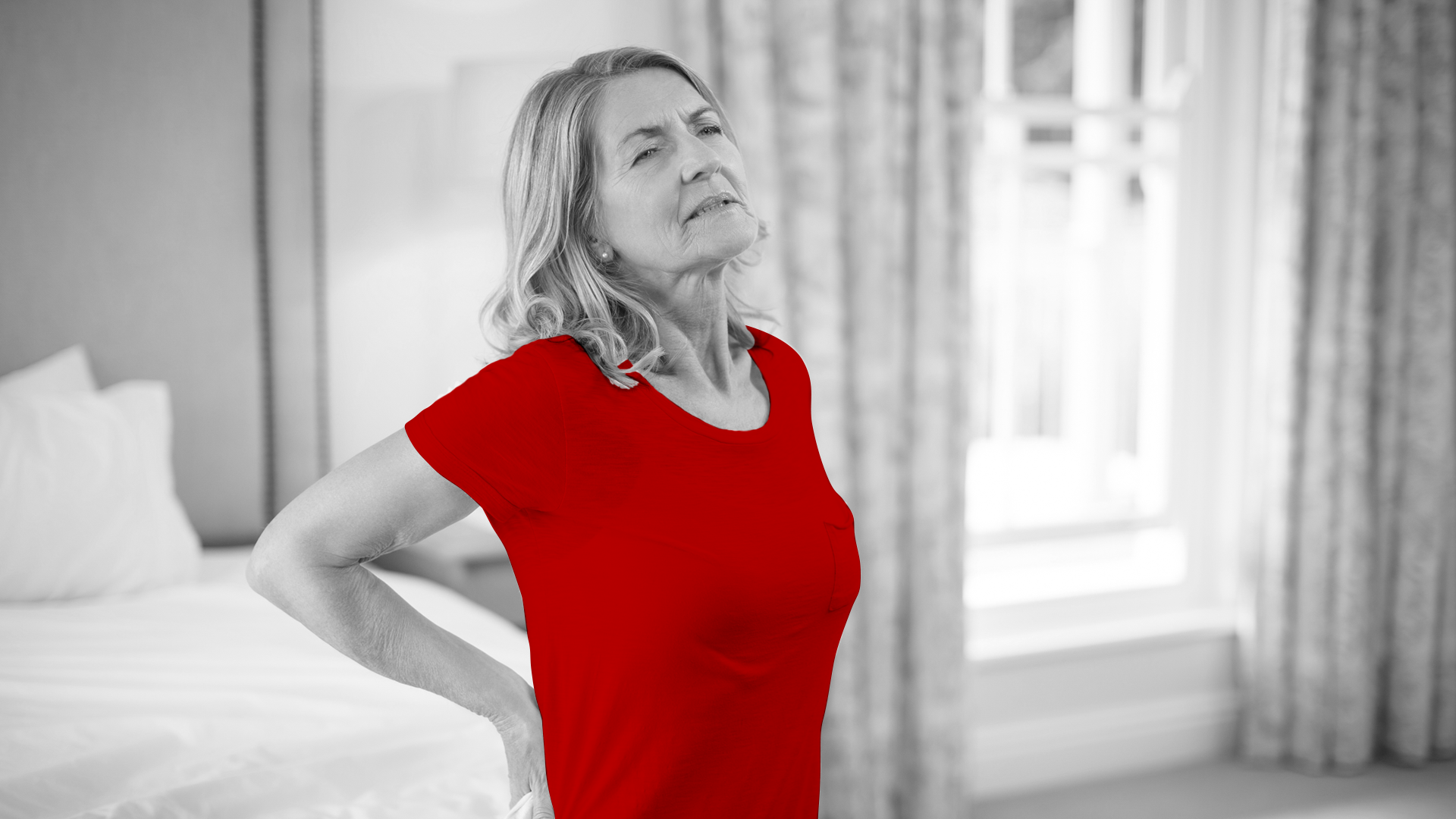 A imagem mostra uma mulher de meia-idade, apoiando a lombar com as mãos, visivelmente sofrendo dores.