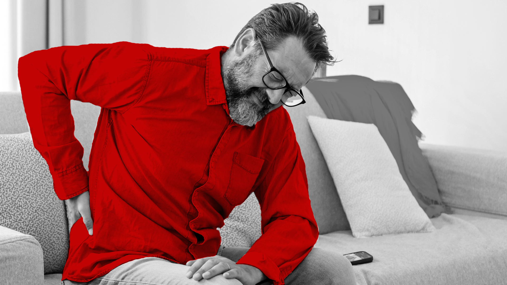 A imagem mostra um homem de meia-idade, sentando em seu sofá, com dores nas costas.