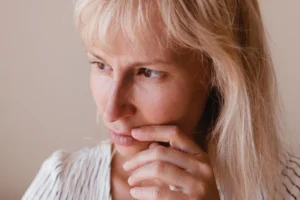 A imagem mostra uma mulher de meia-idade, pensativa, olhando para o horizonte com uma das mãos perto do queixo. Ilustra o texto sobre AIDS.