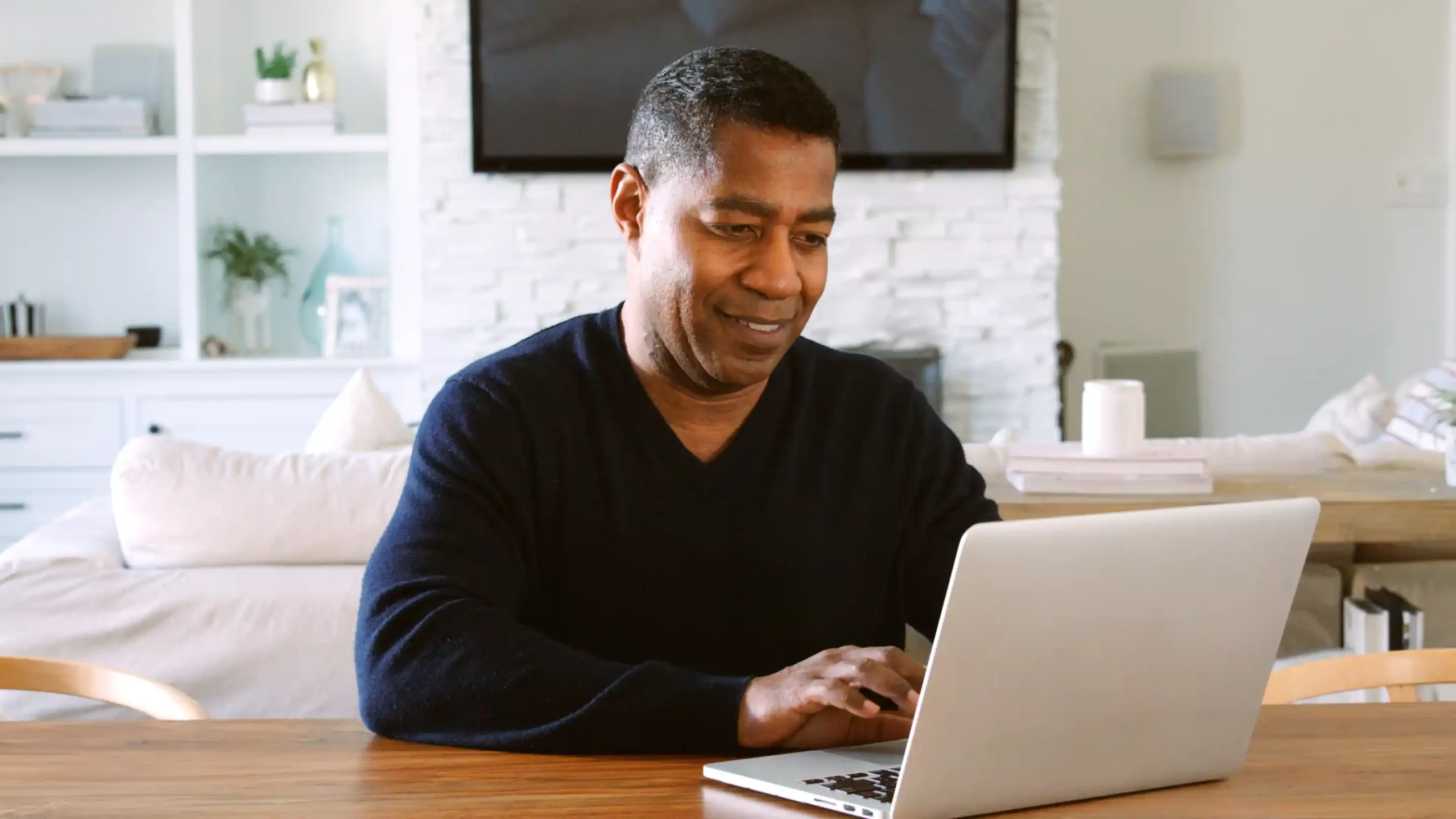 A imagem mostra um homem de meia-idade, sentado à mesa, sorrindo, equanto utiliza o laptop. Ilustra o texto sofre a diferença entre carência e tempo de contribuição.