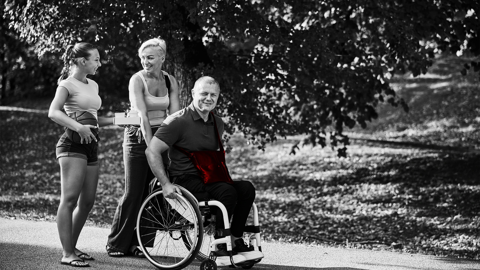 A imagem mostra uma família: filha adolescente e pais de meia-idade, sendo que o pai é cadeirante, passeando por um parque ao ar livre.