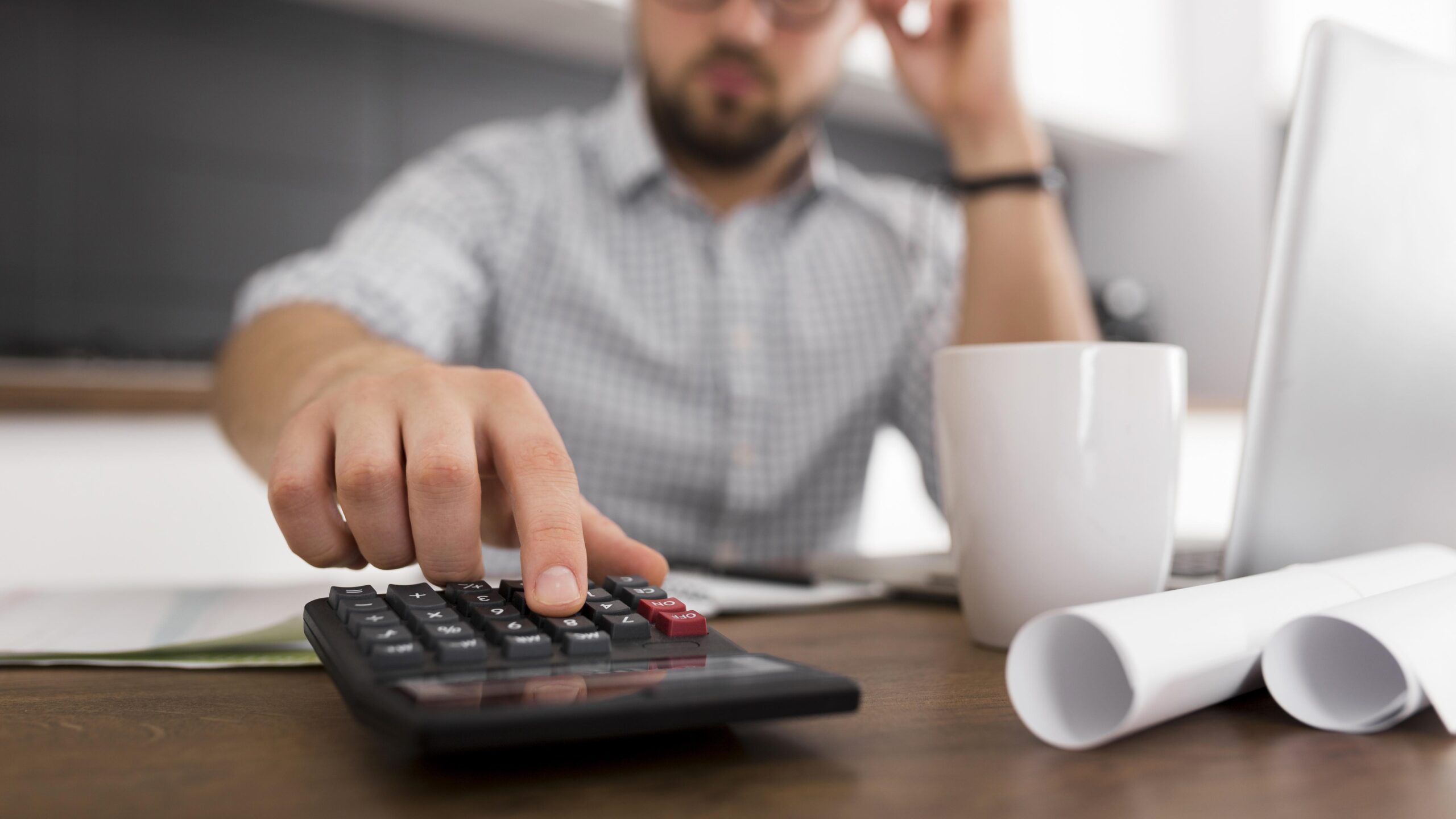 Homem analisando documentos da aposentadoria e cálculo do benefício do INSS em mesa com papéis e calculadora.