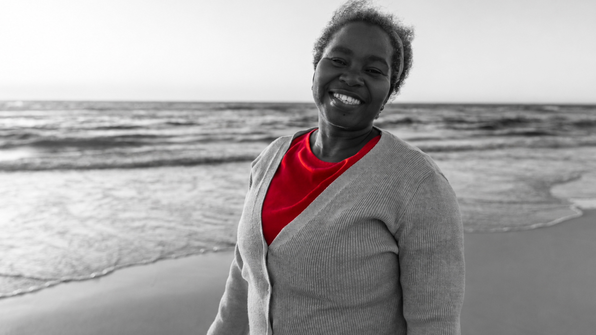A imagem mostra uma mulher de meia-idade, na praia, sorrindo para a câmera.