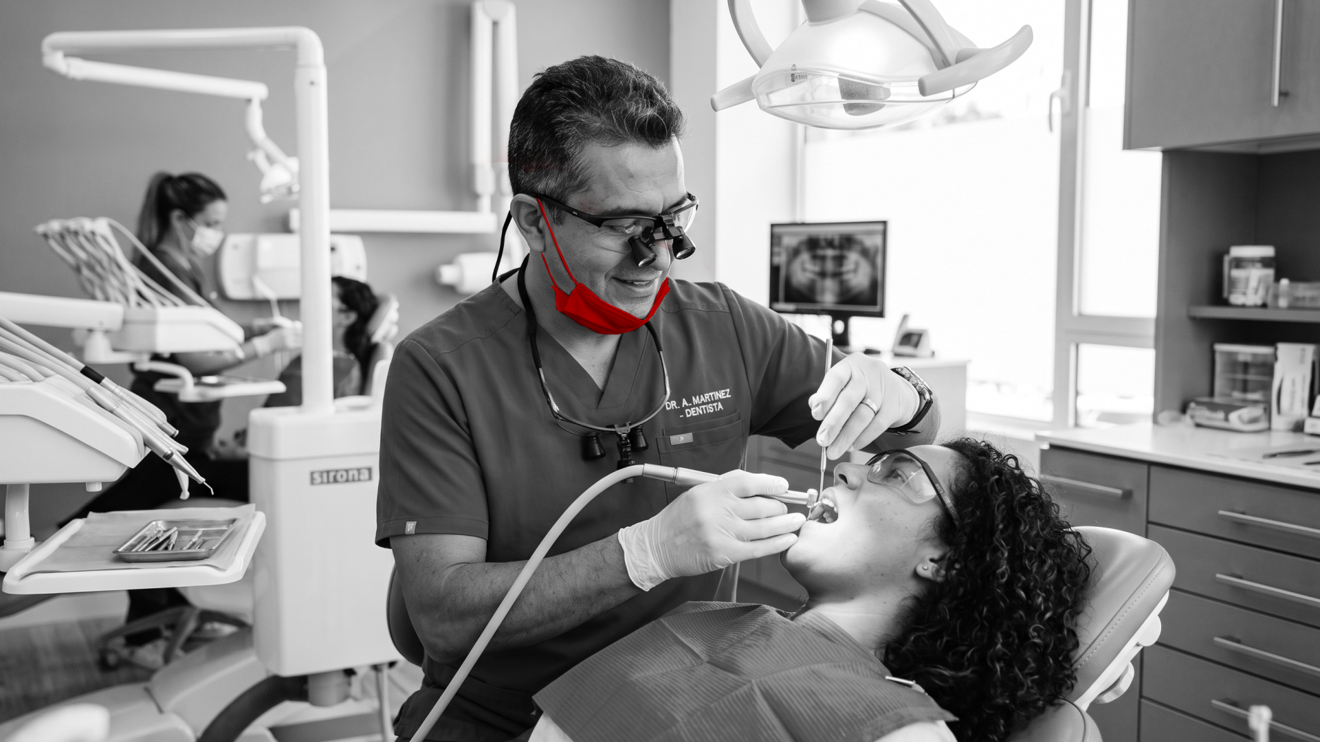 A imagem mostra um dentista de meia-idade, em seu consultório, atendendo uma paciente.