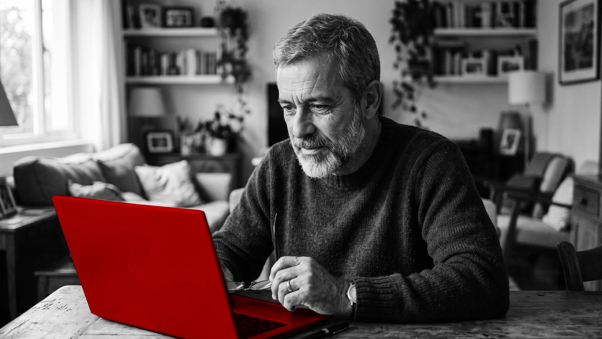 A imagem mostra um homem de meia-idade, sentado à mesa, utilizando um laptop.